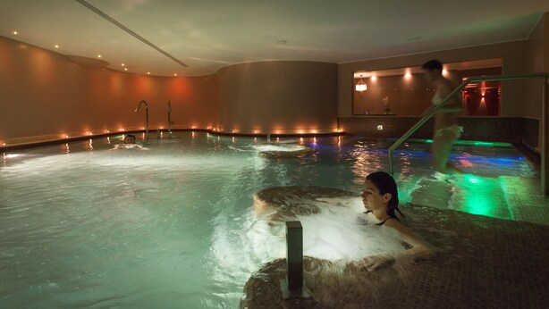 A person in a heated indoor pool with a stone wall and a staircase leading to a higher level. - Ambasciatori Place Hotel (Fiuggi)