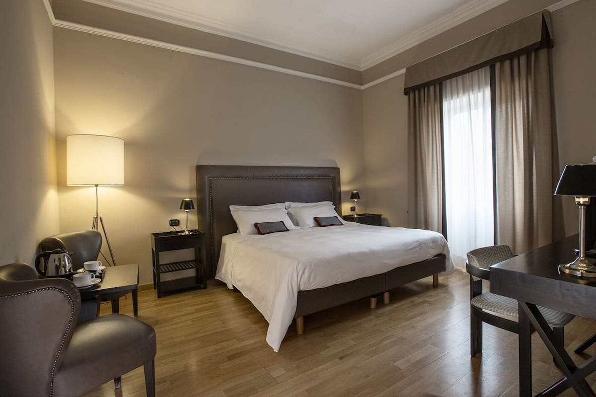 Una habitación de hotel con una cama grande, mesitas de noche, un escritorio y una silla.