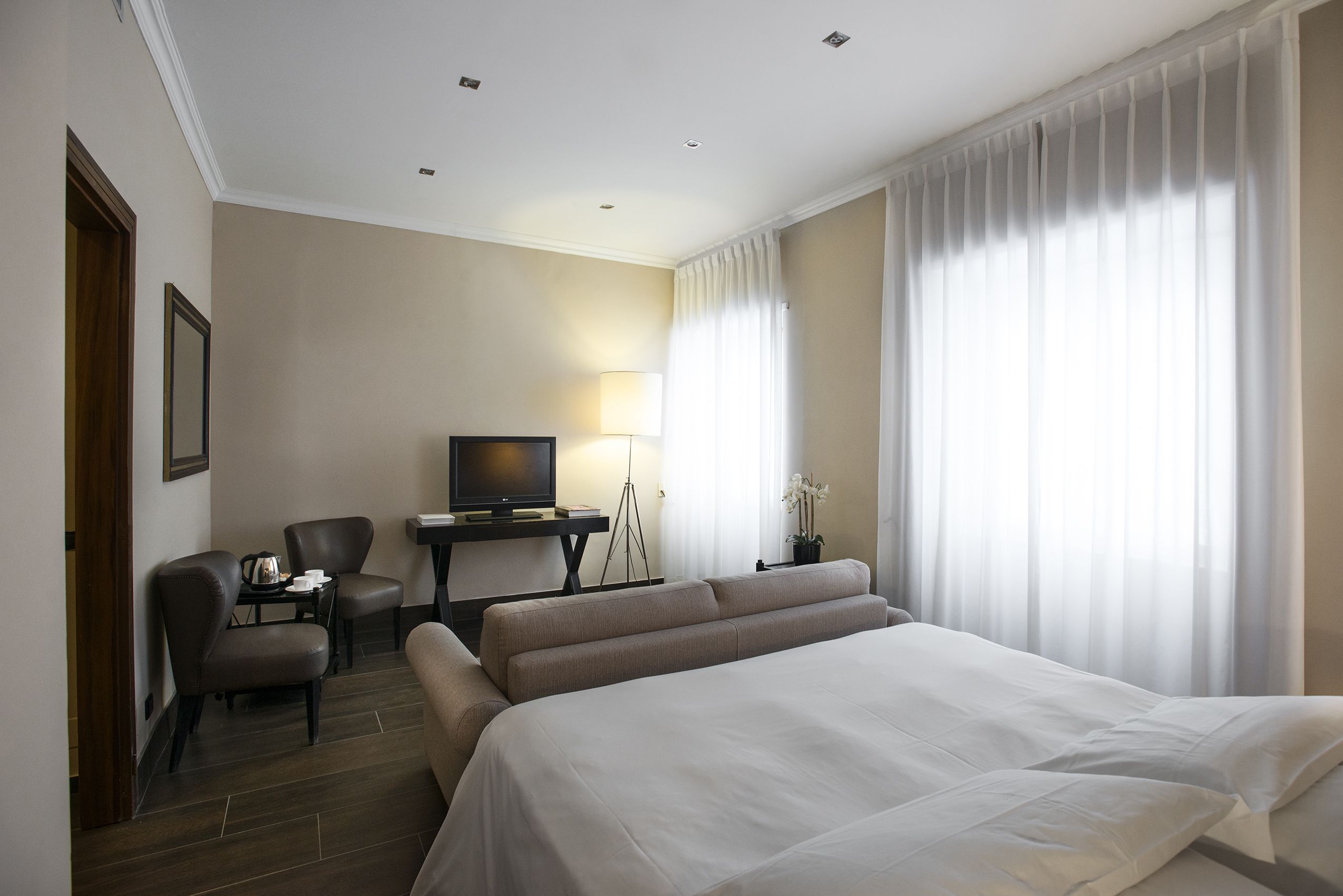 A hotel room with a large bed, a desk with a television, a chair, and a lamp.
