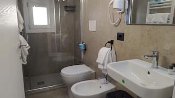 A bathroom with a glass-enclosed shower, a toilet, a bidet, a sink, and a mirror.