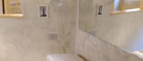 A bedroom with a bed, a wall-mounted light fixture, a mirror, and framed pictures.