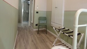 A narrow hallway with a wooden floor, a green chair, a white drying rack, and a white cabinet. - Hotel Santa Croce (Florence)