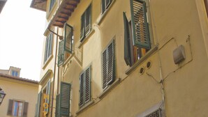 A yellow building with green shutters, a door, and a window with a metal grille. - Hotel Santa Croce (Florence)