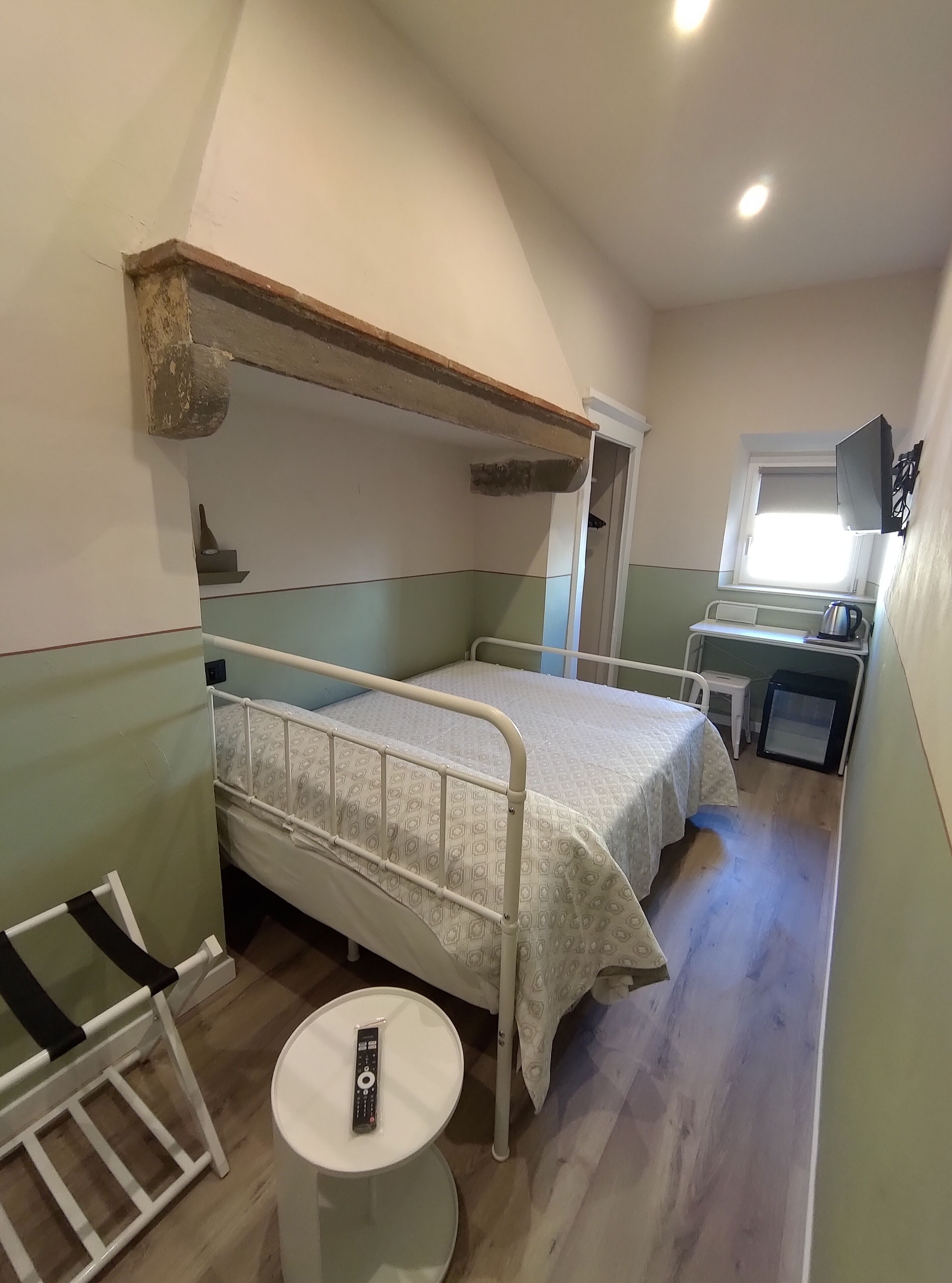 A compact room with a bunk bed, a small table with a remote control, and a kitchenette area with a window.