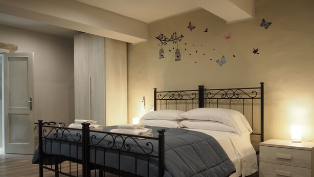 A neatly made bed with a blue blanket and white pillows, a bedside table with a lamp, and a wall with butterfly decals. - Hotel Santa Croce (Florence)