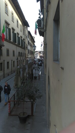 Una calle estrecha flanqueada por edificios, con mesas al aire libre y sombrillas, y algunas personas caminando.