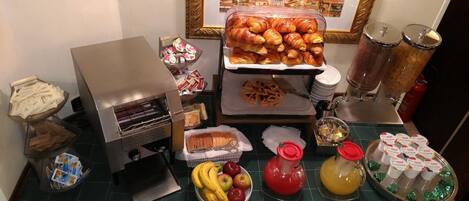 A breakfast buffet with croissants, pastries, fruits, and beverages.