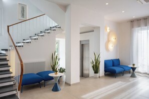 A modern living room with a staircase, blue sofas, a round coffee table, and potted plants. - Hotel Venere Azzurra (Lerici)