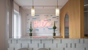 A modern kitchen with a neon 'Hello' sign, two bar stools, and a tiled backsplash. - Hotel Venere Azzurra (Lerici)