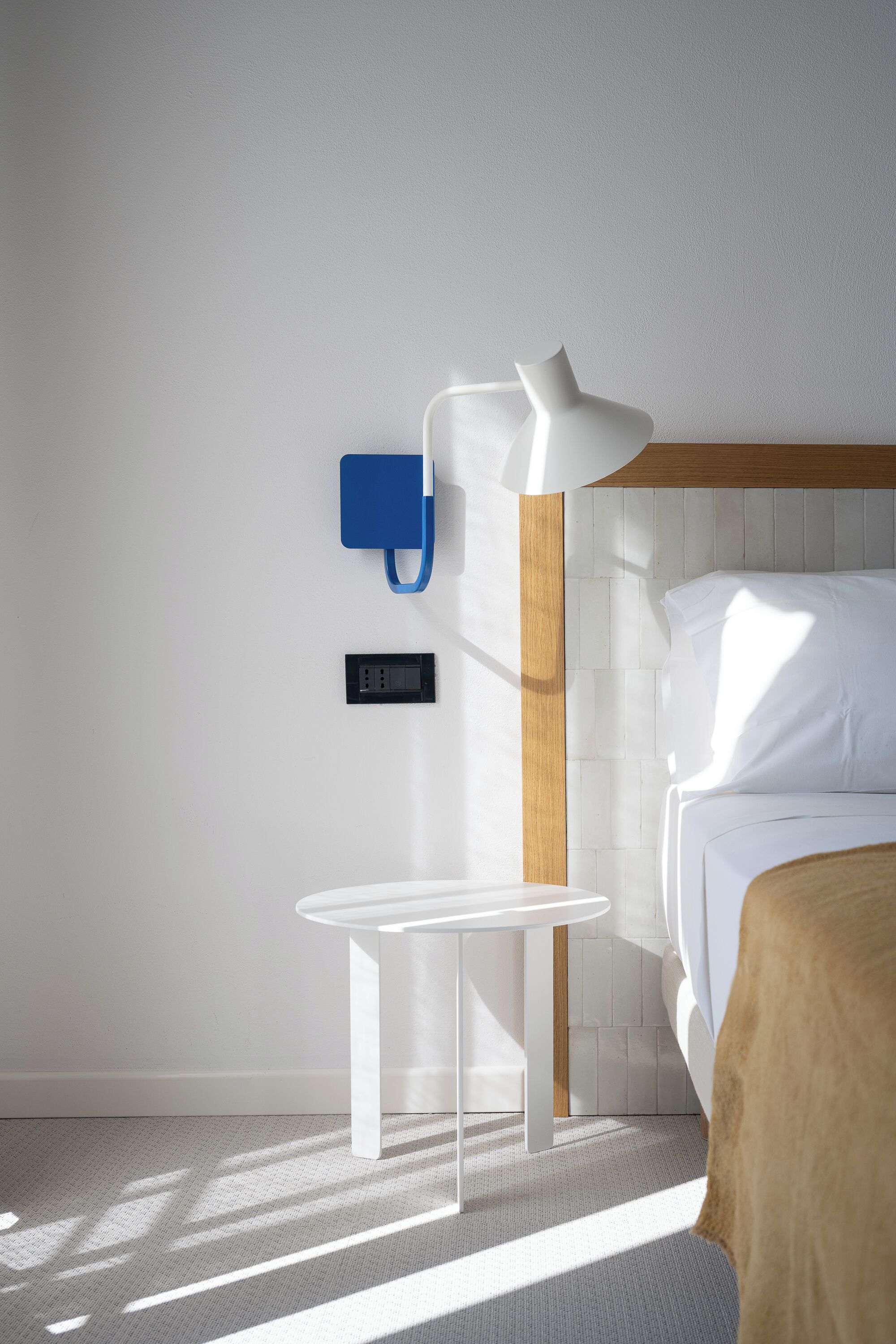 Een moderne hotelkamer met een bed, nachtkastje, lamp en een stopcontact.