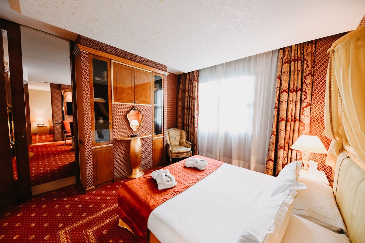 A hotel room with a bed, a wardrobe, a chair, and a desk with a lamp.