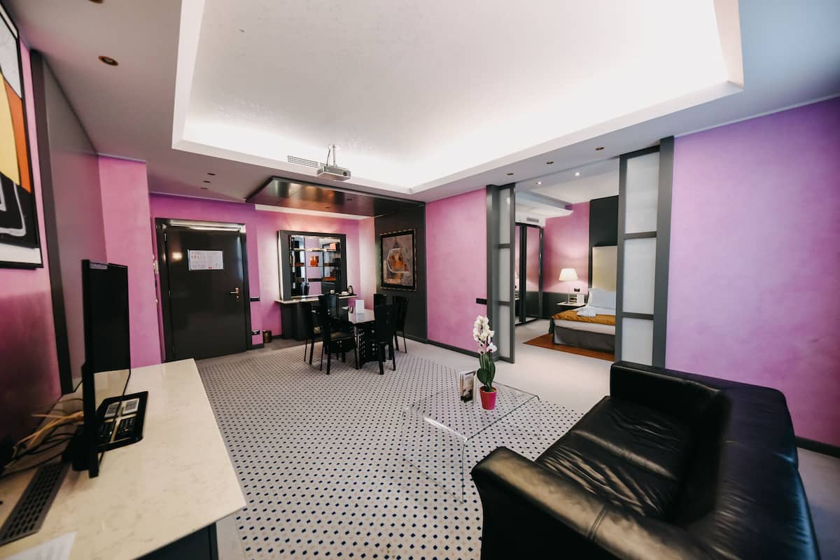 A modern hotel lobby with a black leather sofa, a reception desk, and a dining area with chairs and a table.