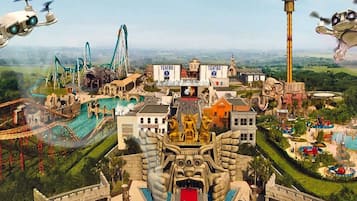 Un parque temático con diversas atracciones, entre ellas montañas rusas, una noria y una estatua imponente.
