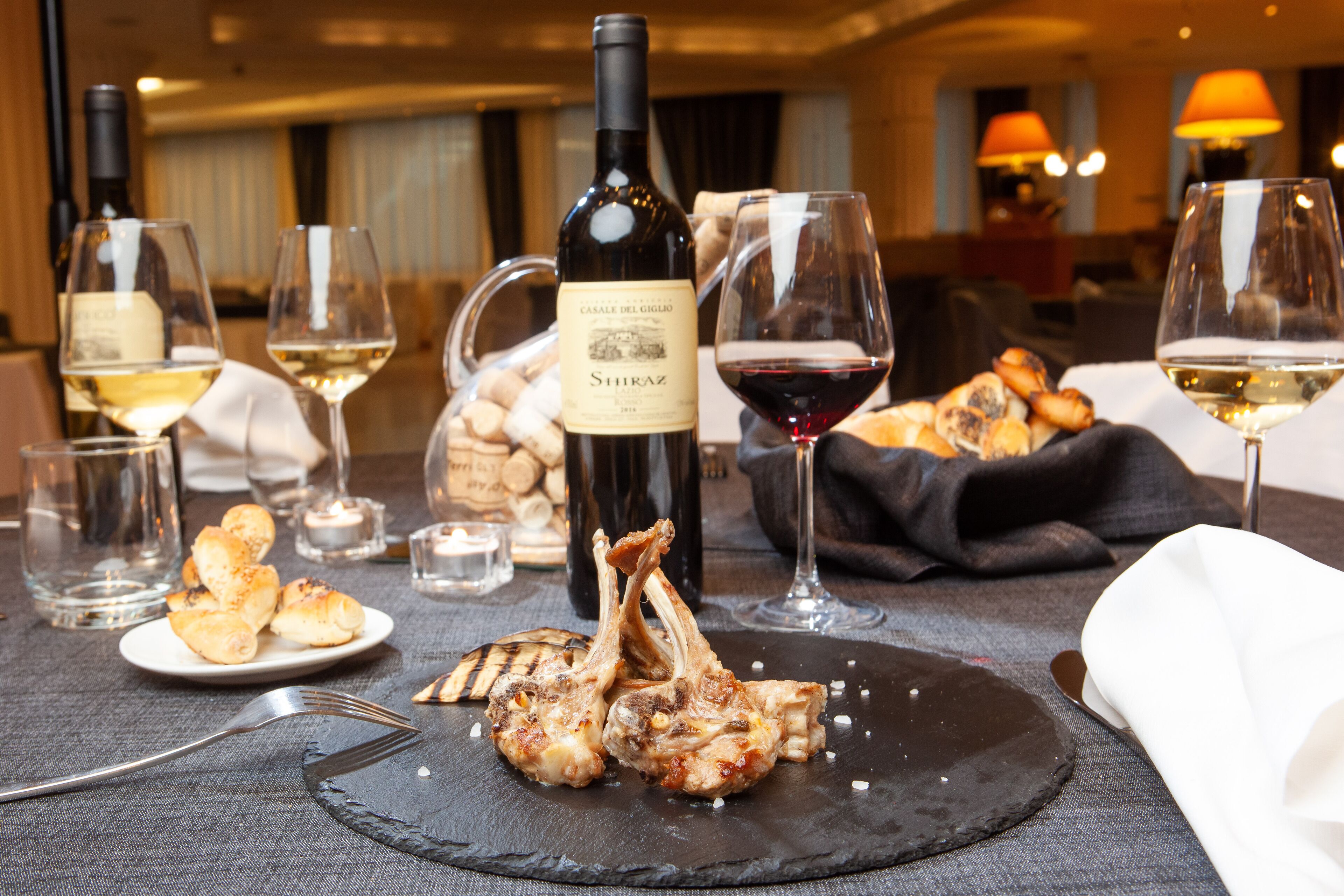 A dining table with a bottle of wine, glasses, a plate of food, and a fork.