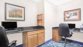 A small office with two desks, each with a computer and keyboard, and a chair. There are framed pictures on the walls and a patterned carpet.