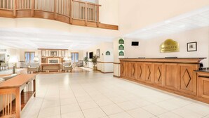 A spacious lobby with a wooden reception desk, seating area, and a staircase leading to an upper level.