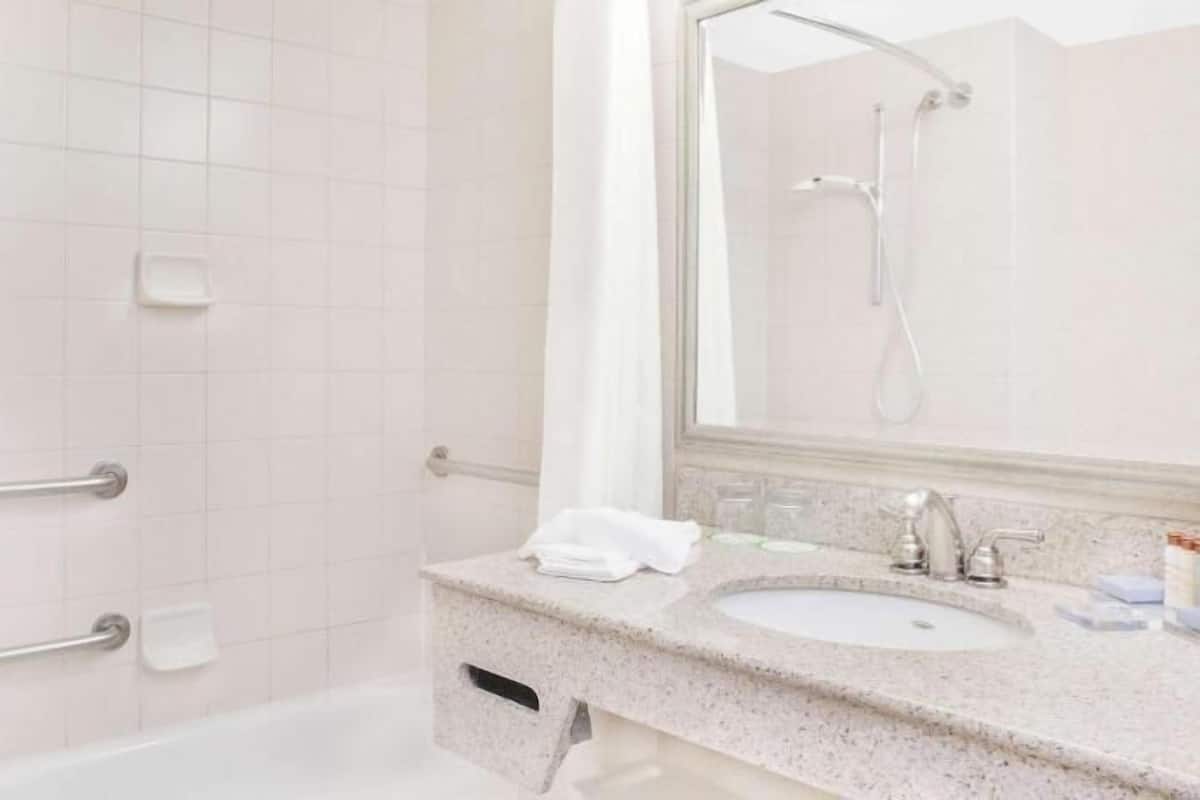 A bathroom with white tiles, a bathtub, a sink with a mirror, and a shower.