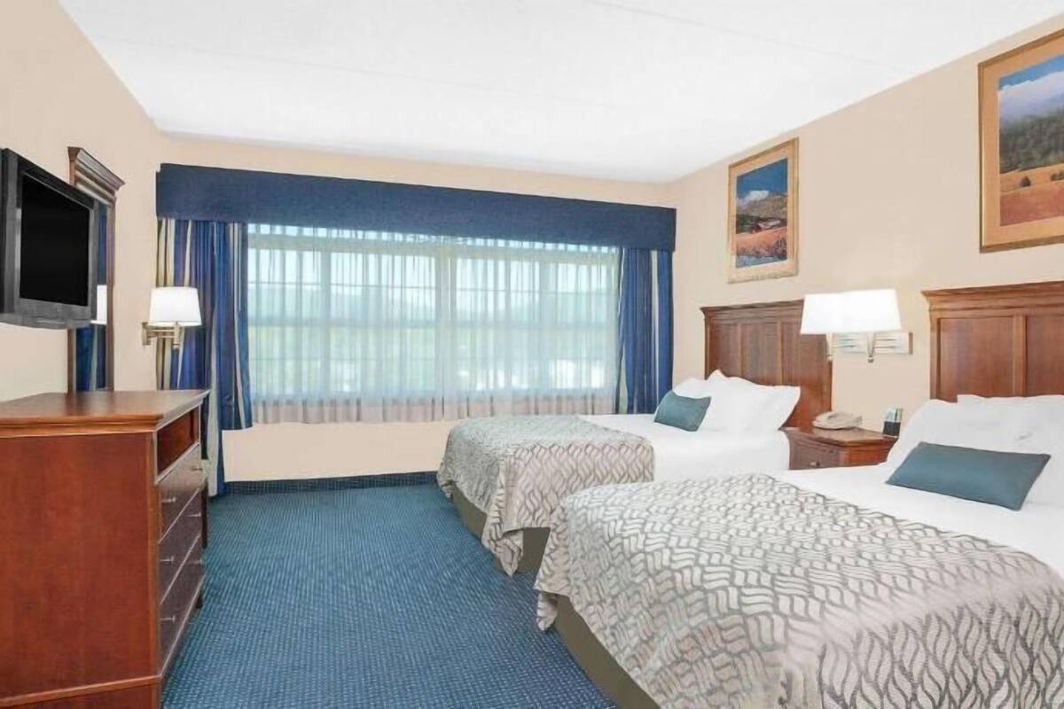A hotel room with two beds, a TV, a desk, and a window with curtains.