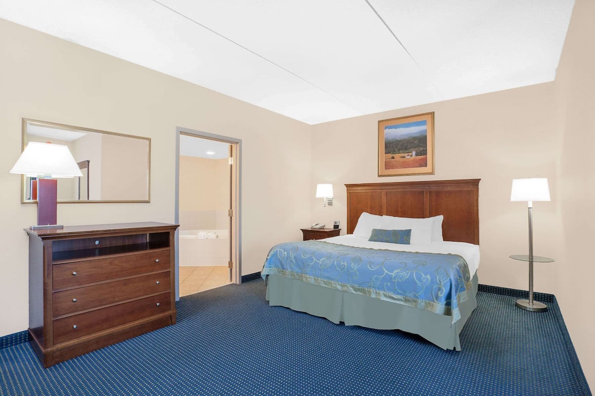 A hotel room with a bed, a dresser, a nightstand, a lamp, and a painting on the wall.