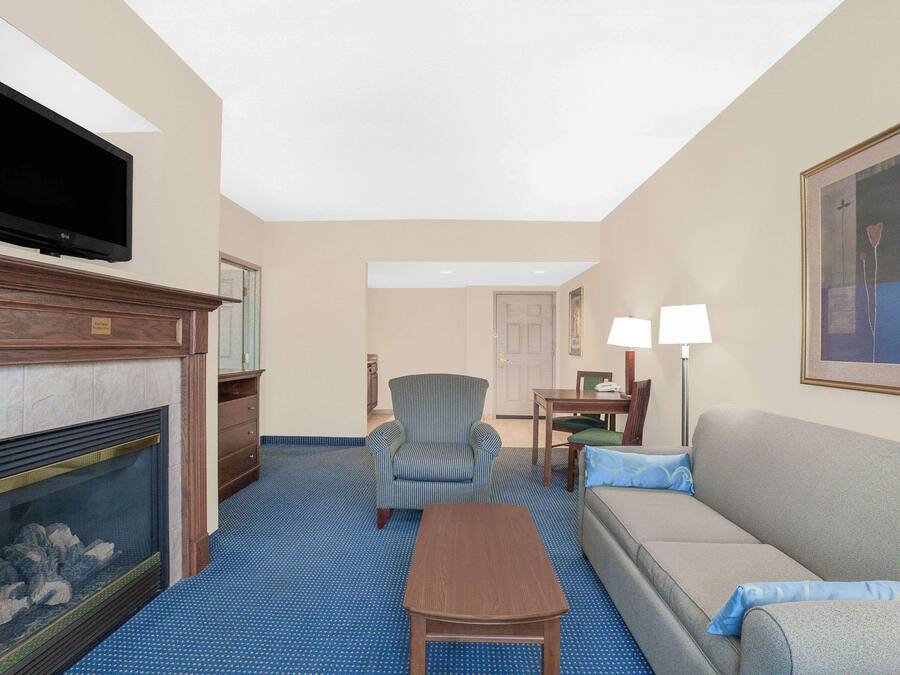A hotel room with a fireplace, a television mounted on the wall, a striped armchair, a sofa, a small table, and a painting on the wall.
