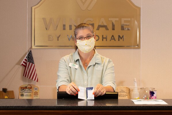 A receptionist at a hotel counter with a sign reading "Wingate by Wyndham" in the background.
