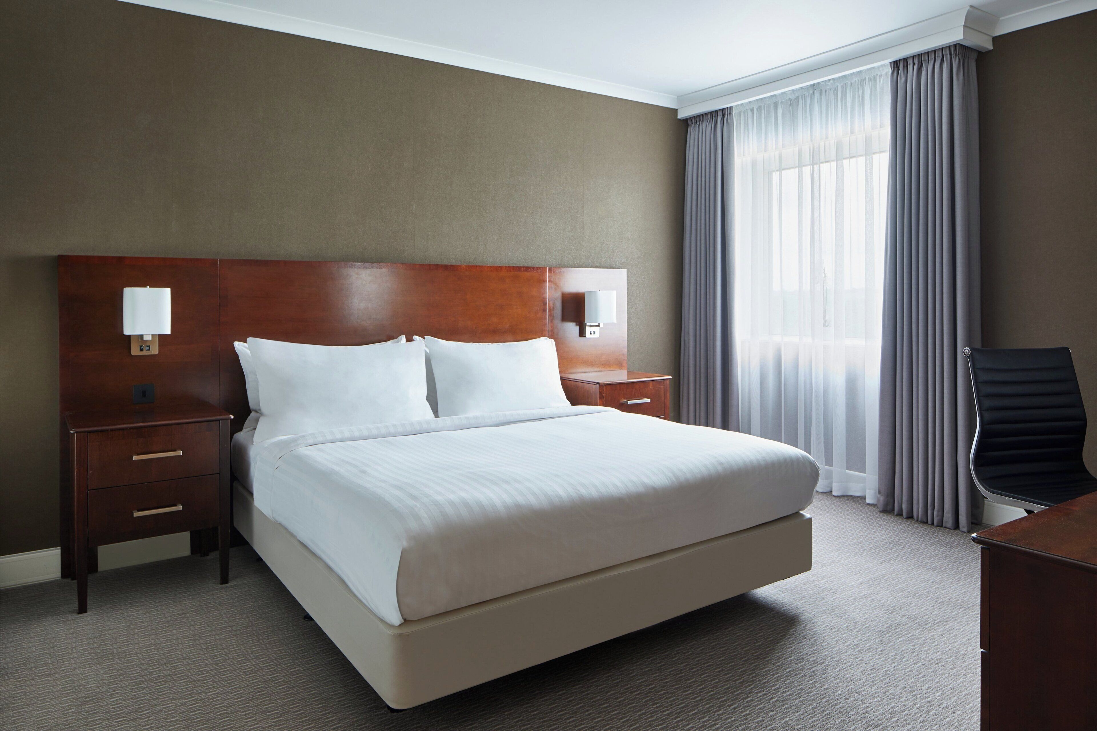 A hotel room with a large bed, two bedside tables, a desk, and a chair.