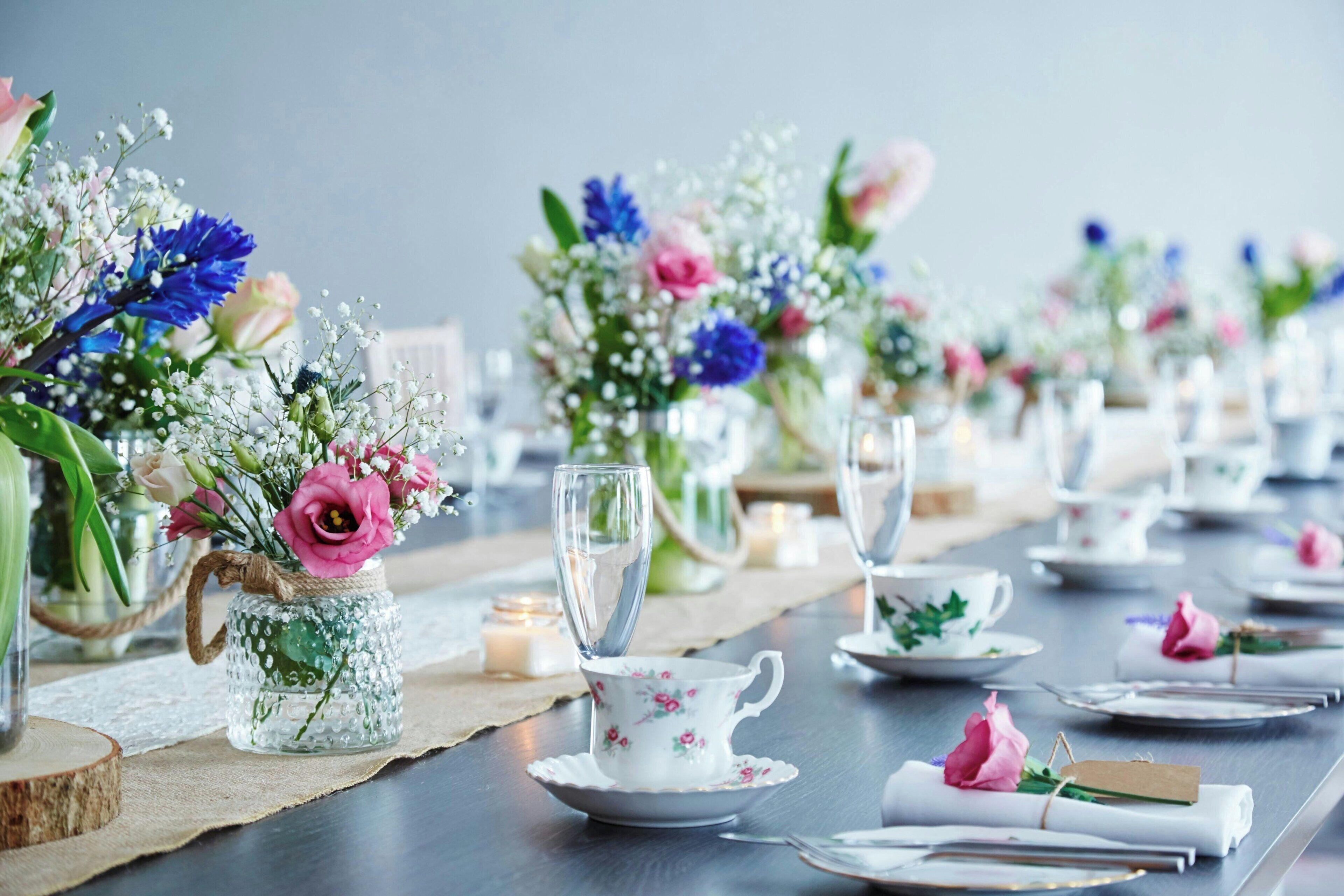 A table set with floral centerpieces, white teacups, and saucers.