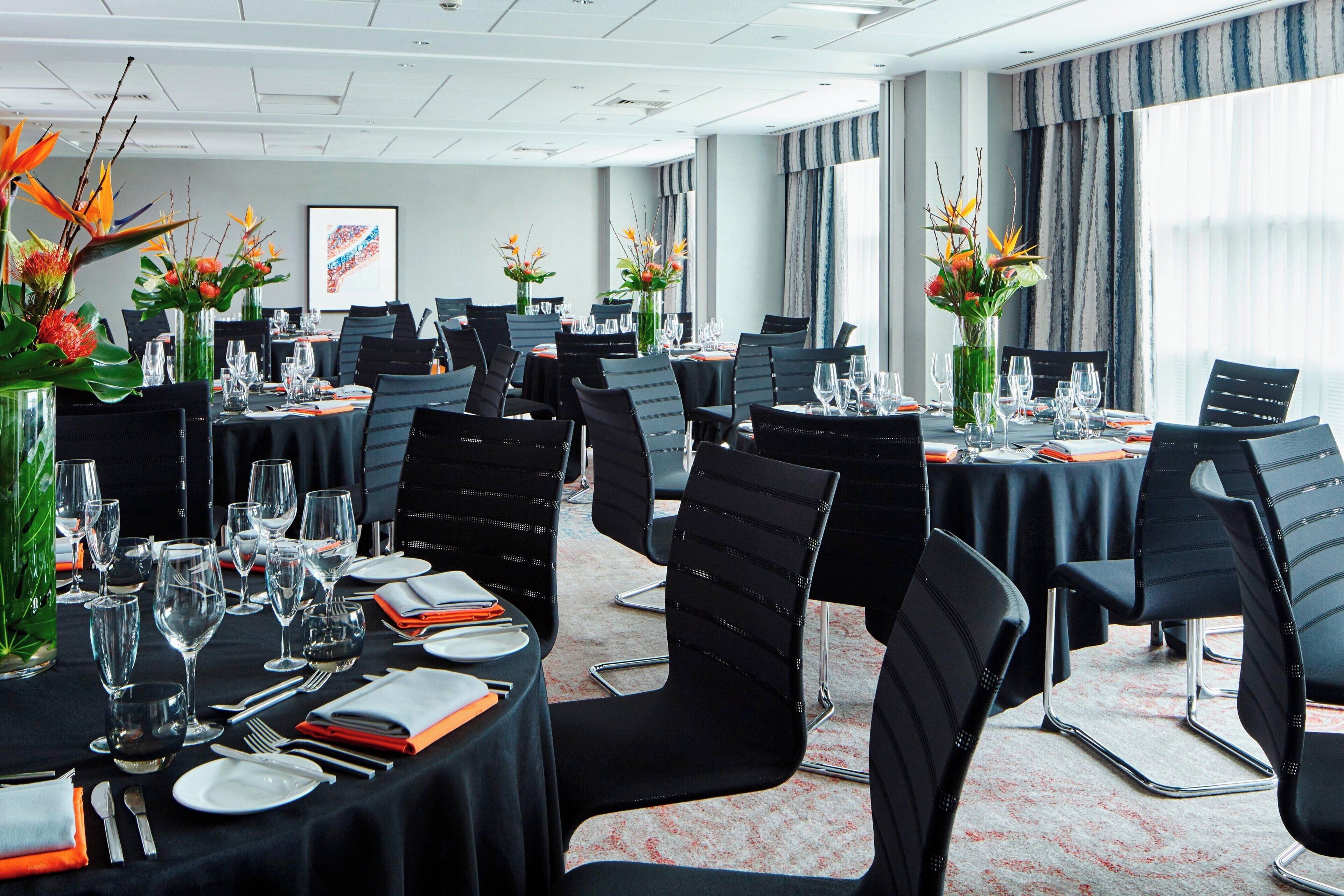 A conference room with round tables, black chairs, and floral centerpieces.