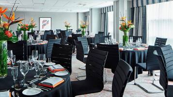 Une salle de conférence avec des tables rondes, des chaises noires et des arrangements floraux en guise de décoration centrale.