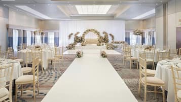 A banquet hall with a central aisle, round tables, and a floral arch at the end.