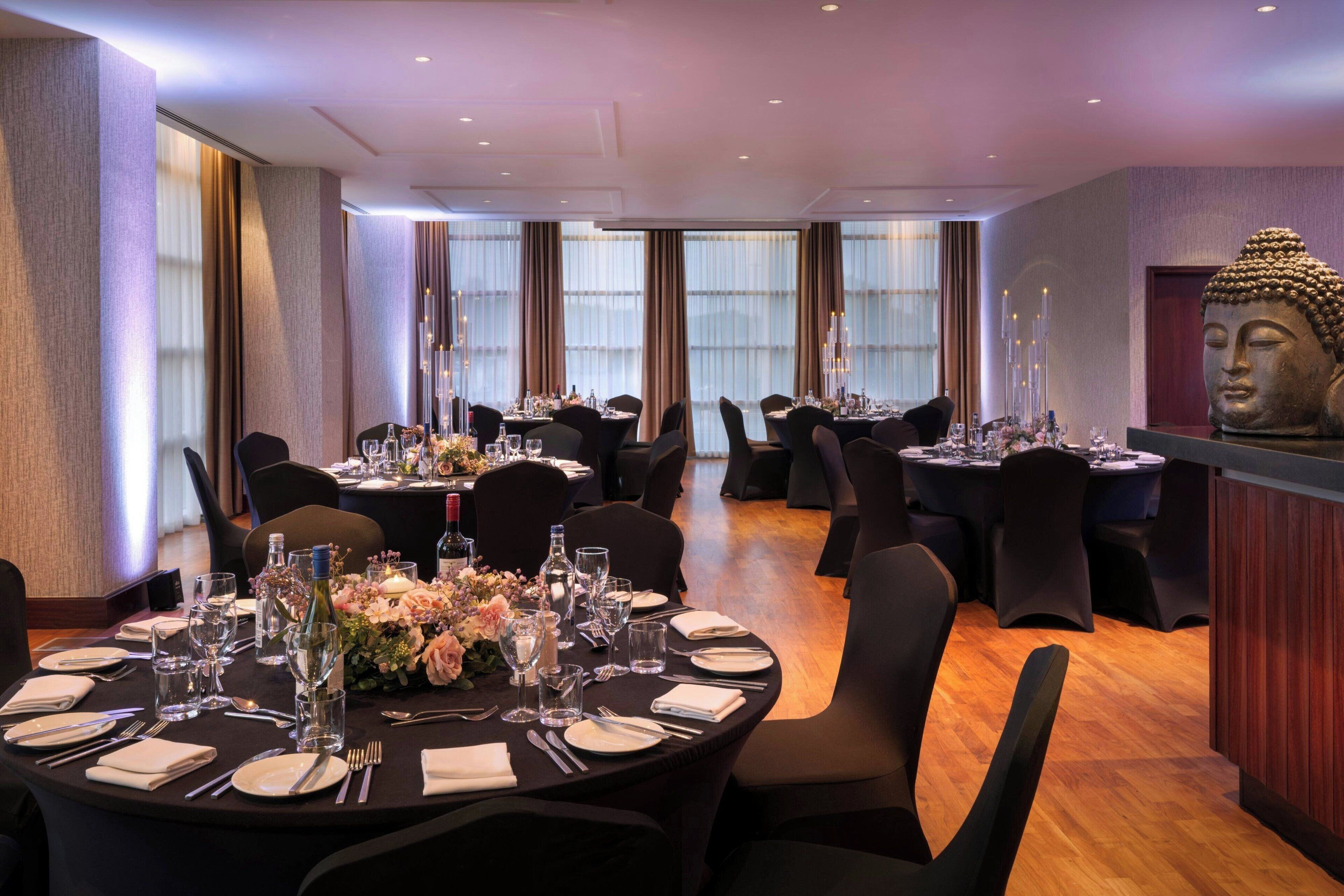 A dining area with round tables set for four, each with a vase of flowers, wine glasses, and cutlery.