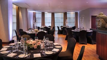 A dining area with round tables set for four, each with a vase of flowers, wine glasses, and cutlery.