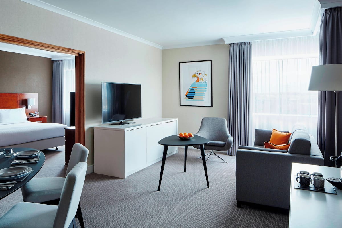 A hotel room with a bed, a desk, a television, a framed picture, a sofa, and a dining area.