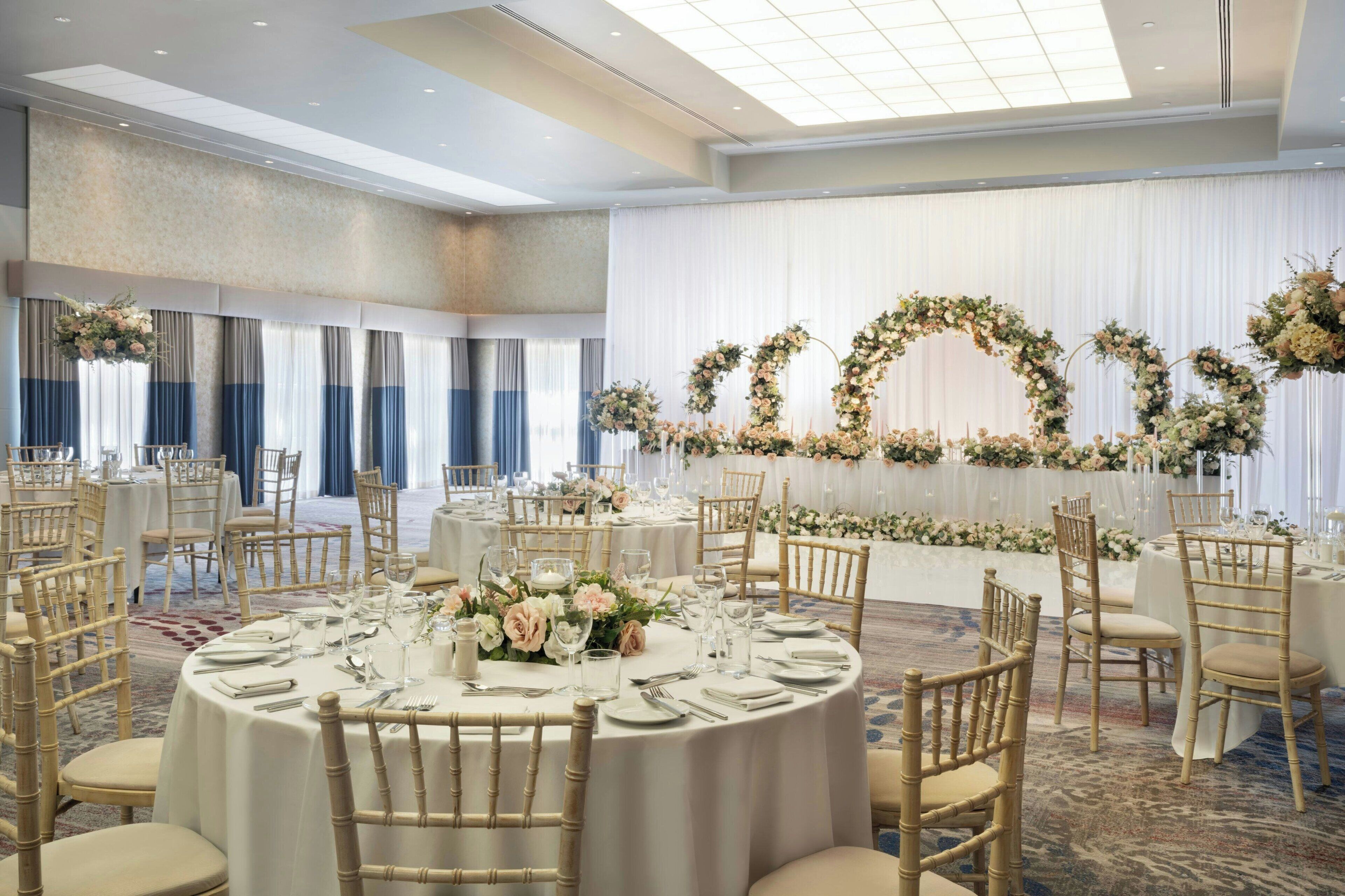 A banquet hall with round tables set for a formal event, featuring white tablecloths and floral centerpieces.