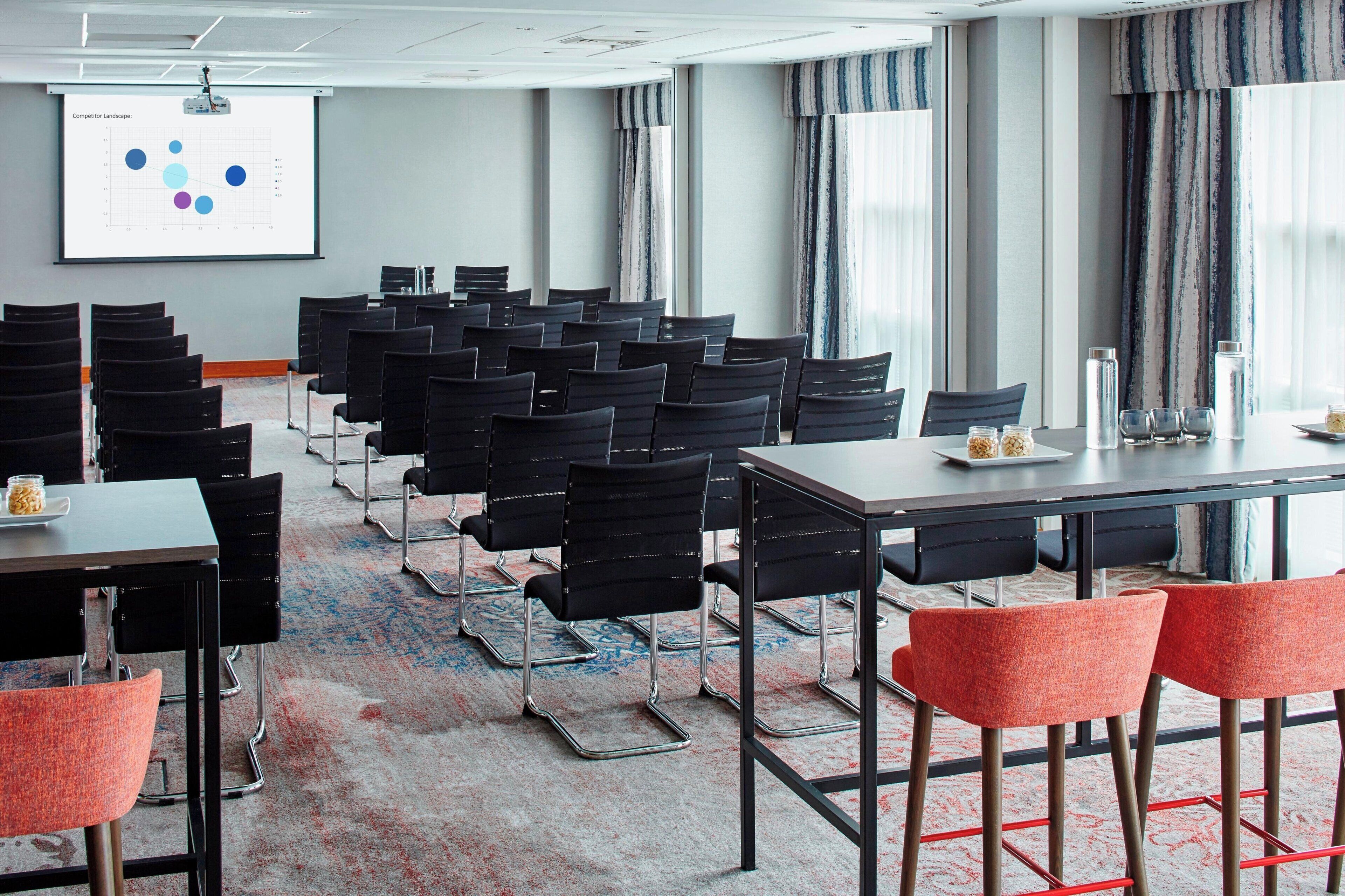 A conference room with rows of black chairs, a large screen displaying a graph, and a carpeted floor.