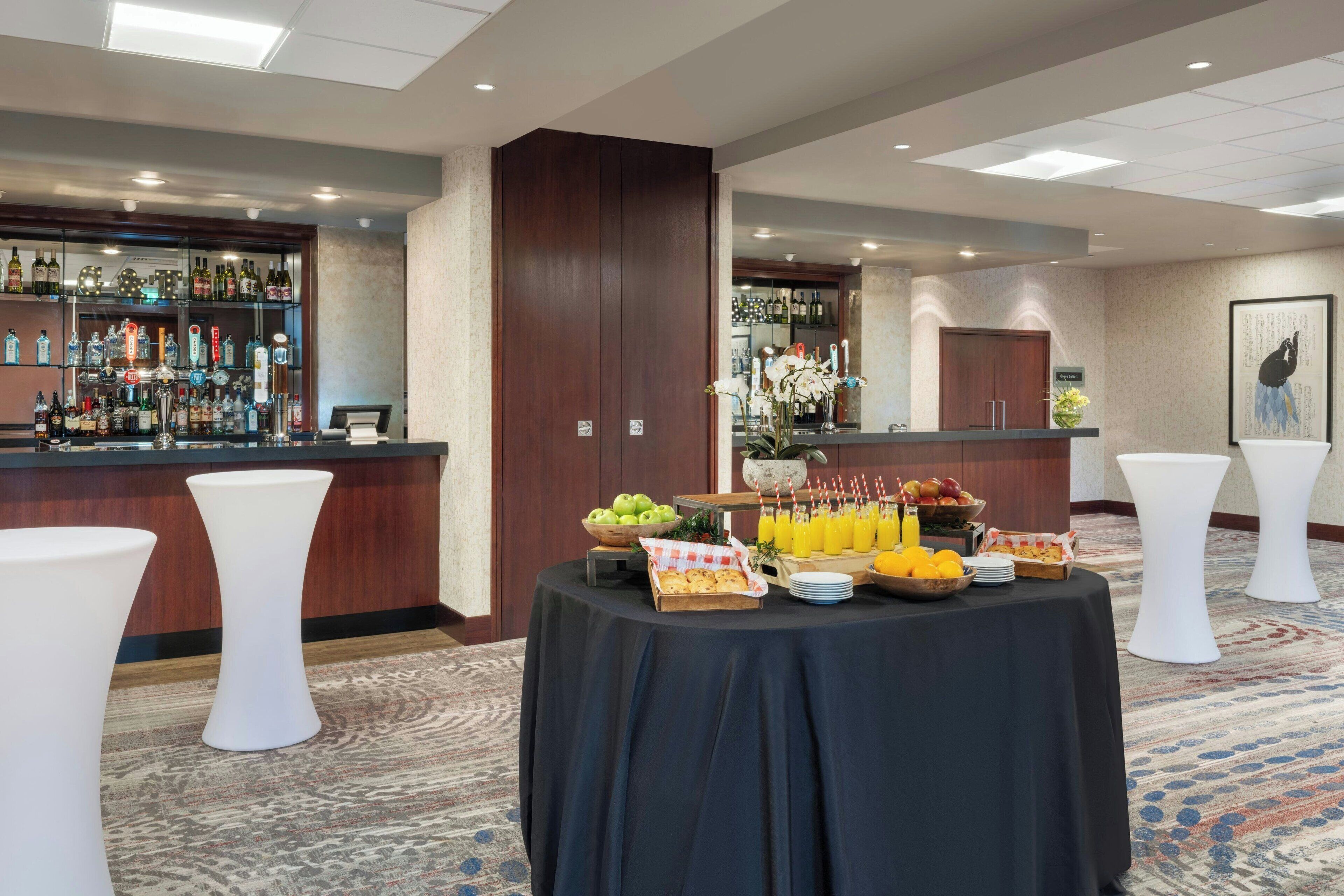 A bar area with a variety of liquor bottles, a fruit bowl, and a tray of orange juice.