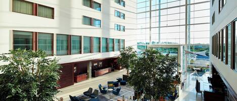 A spacious indoor area with multiple seating arrangements, large windows, and indoor plants.