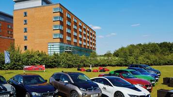 A row of parked cars in front of a modern building with a brick facade and large windows.