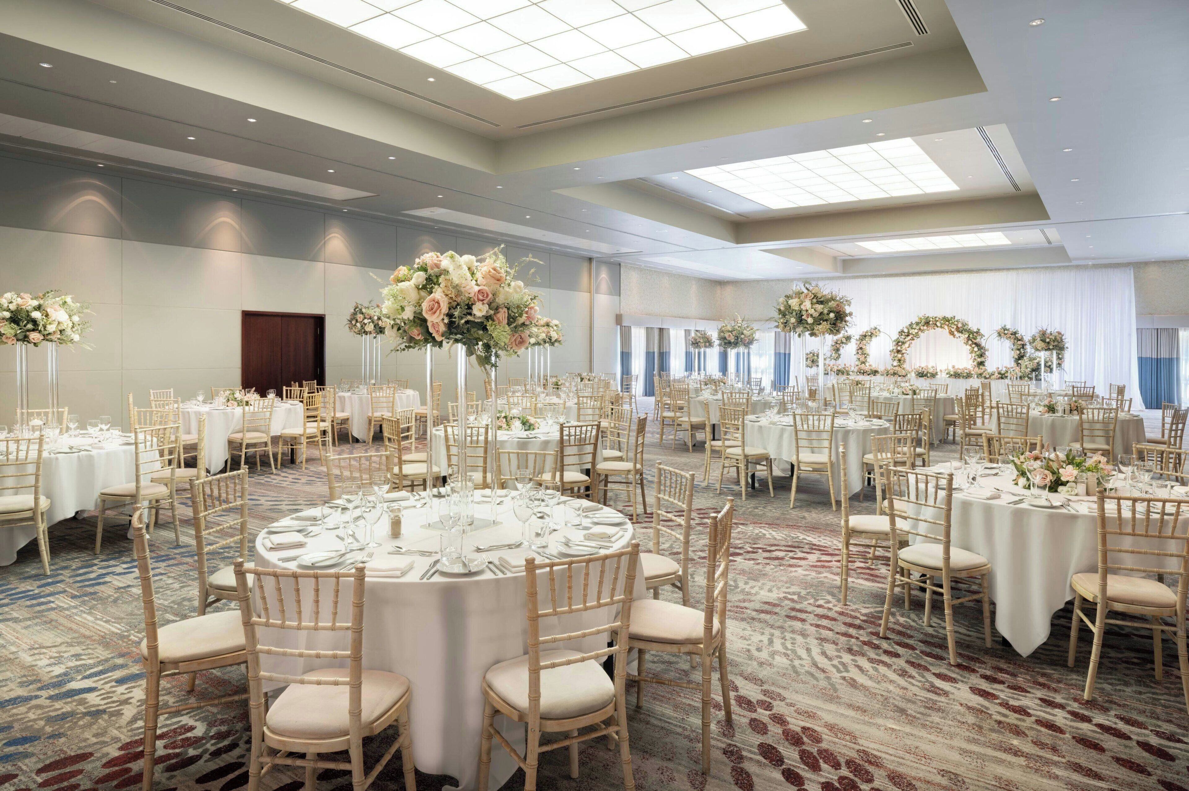 A large banquet hall with round tables, white tablecloths, and gold chairs.