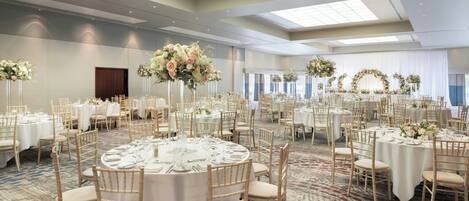 A large banquet hall with round tables, white tablecloths, and gold chairs.
