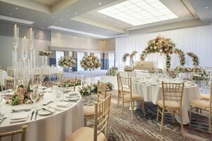 A banquet hall with round tables, tall candle-like fixtures, and floral centerpieces.