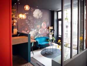 A modern interior with a blue sofa, a wooden table, and a mural of flowers. - Ibis Styles Paris Batignolles (Paris)