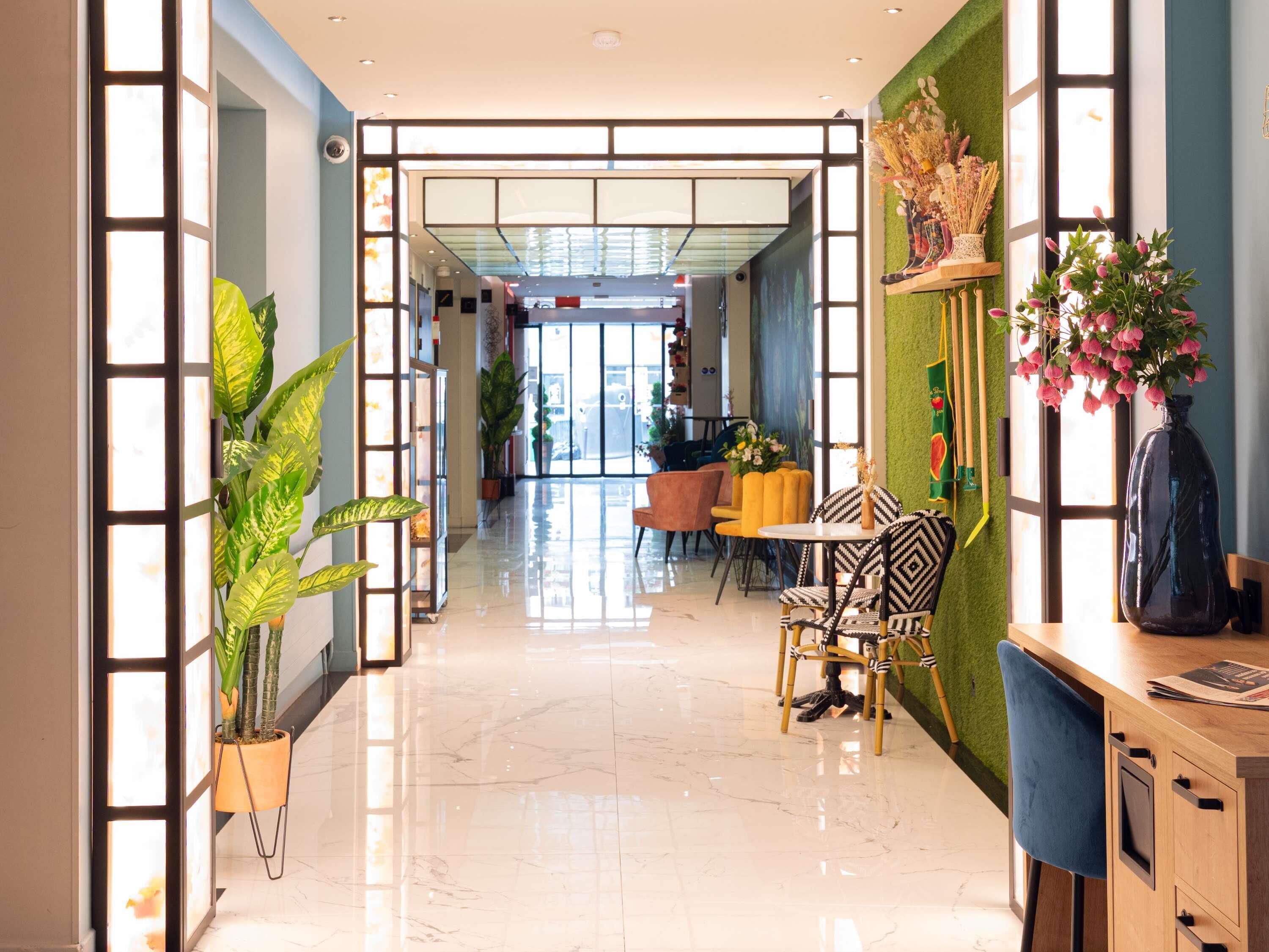 A modern hotel lobby with a glass partition, a reception desk, and a dining area with chairs and a table.