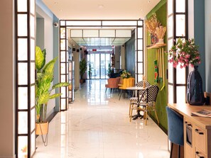 A modern hotel lobby with a glass partition, a reception desk, and a dining area with chairs and a table. - Ibis Styles Paris Batignolles (Paris)