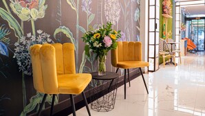 A modern interior with two yellow velvet chairs, a round table with a geometric wire base, and a floral mural on the wall. - Ibis Styles Paris Batignolles (Paris)