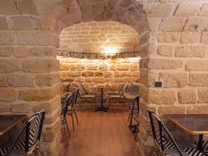 An interior with stone walls, wooden flooring, and patterned chairs around tables. - Ibis Styles Paris Batignolles (Paris)
