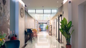 A hotel corridor with a modern design, featuring a glass ceiling, a clock, and a seating area with chairs and tables. - Ibis Styles Paris Batignolles (Paris)