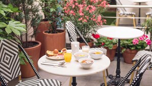 A round table with breakfast items, surrounded by potted plants and wicker chairs. - Ibis Styles Paris Batignolles (Paris)