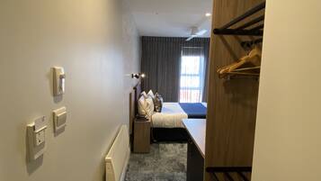 A hotel room with a bed, a bedside table, a nightstand, a wardrobe, and a bathroom with a shower.