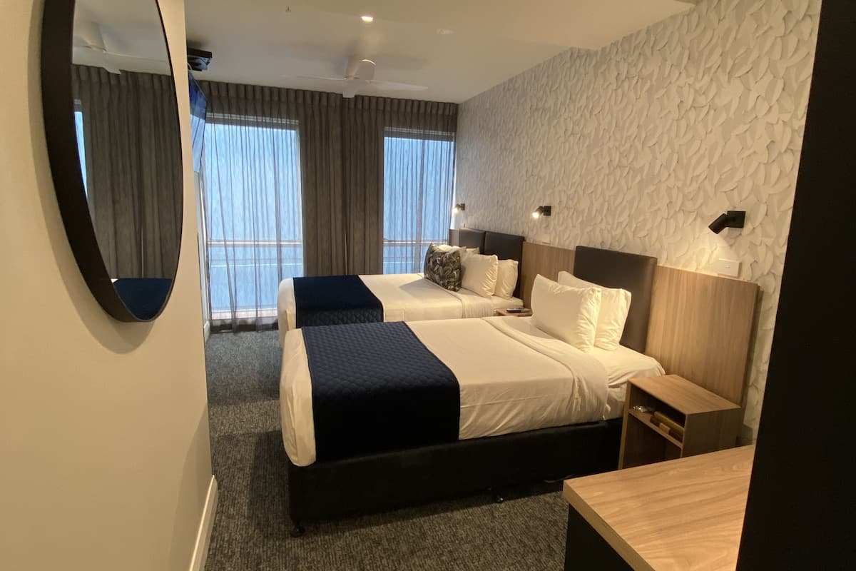 Ein Hotelzimmer mit zwei Betten, einem großen Spiegel, einem Deckenventilator und einer Wand mit Struktur.